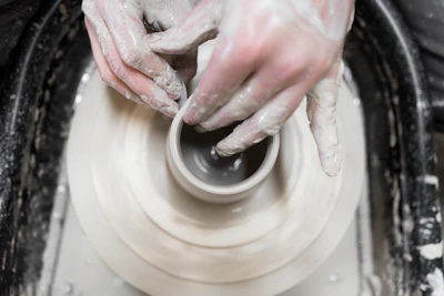An artist’s hands shaping a clay pot on a spinning wheel, with splashes of bright glaze nearby.