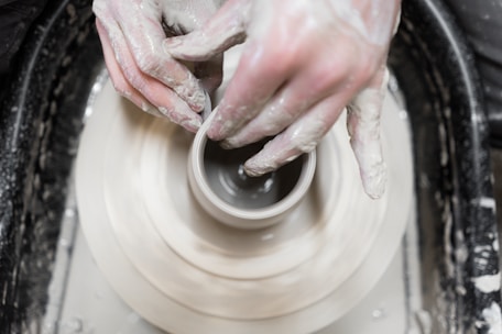 Close-up of a craftsman shaping a clay pot with hands covered in wet clay.