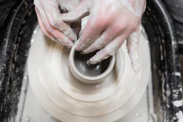 An artisan shaping clay on a pottery wheel, hands covered in wet clay.