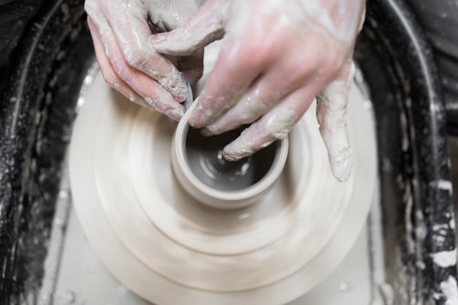 Hands shaping clay in a pottery workshop environment.