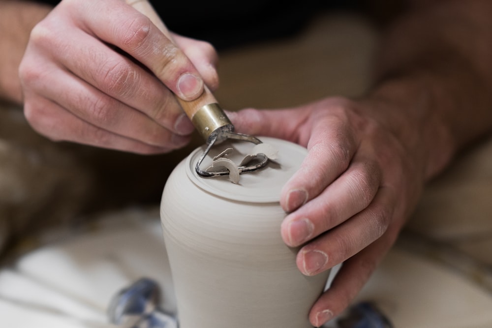 Persona che tiene in mano un vaso in ceramica bianca con coperchio argento e oro