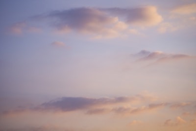 Soft, fluffy clouds float across a gentle, pastel-colored sky with hues of pink, purple, and blue.