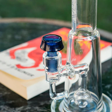 Close-up of a sleek borosilicate glass pipe resting on a dark reflective surface with soft lighting.