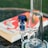 A close-up of a glass bong with a blue accented mouthpiece, placed on a table. In the background, a blurred book with a vibrant red and white cover is visible.