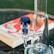 A close-up of a glass bong with a blue accented mouthpiece, placed on a table. In the background, a blurred book with a vibrant red and white cover is visible.