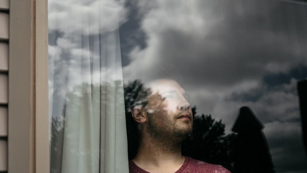 man in red crew neck shirt standing near white curtain