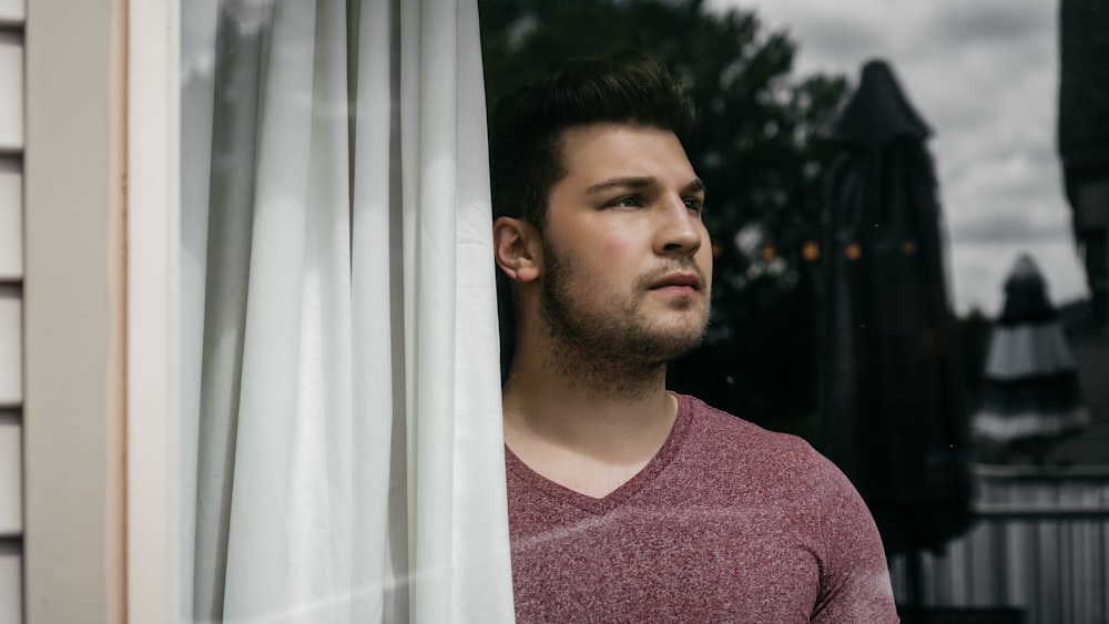 man in red crew neck shirt standing beside white curtain