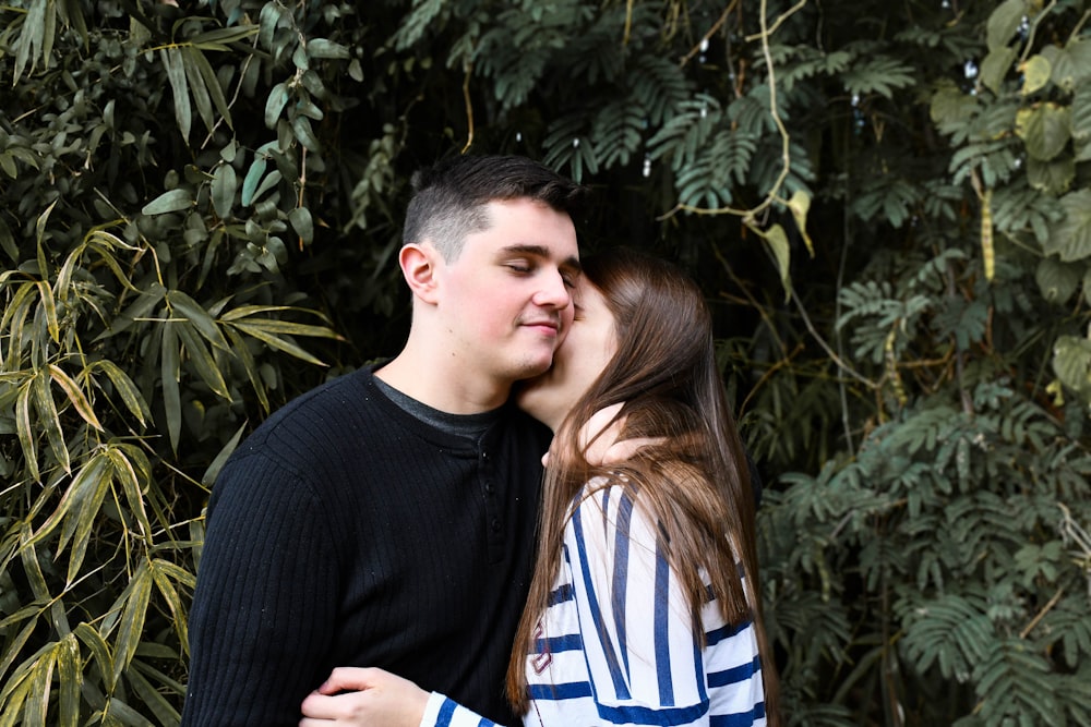 man in black sweater kissing woman in blue and white striped shirt