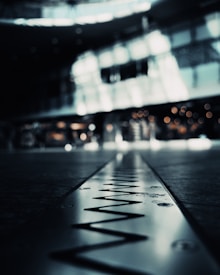 A metal strip with a zigzag pattern is prominently displayed in the foreground, with a blurred background that suggests an indoor setting with bright lighting and soft bokeh effects.