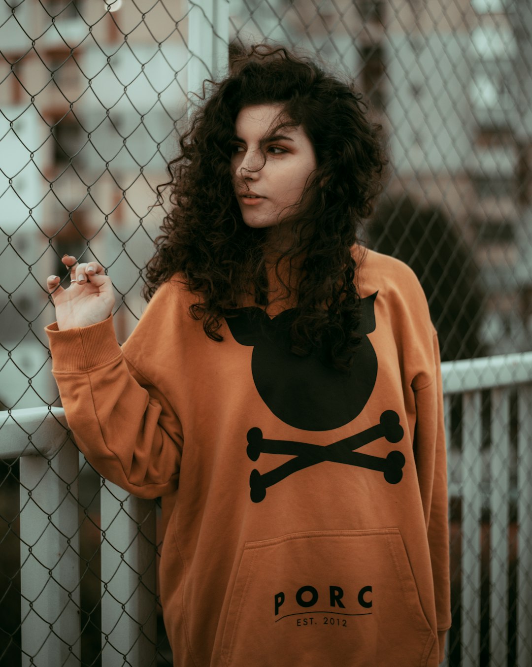 woman in orange and black long sleeve shirt standing beside gray metal fence during daytime