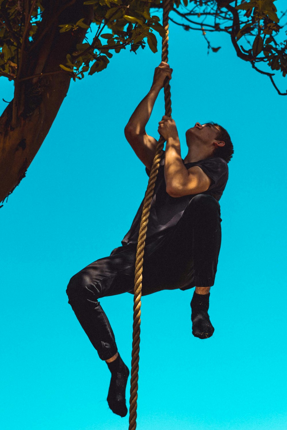Mann in schwarzem Tanktop und schwarzer Hose klettert an braunem Seil