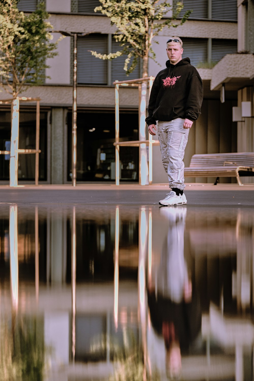 man in black hoodie and white pants standing on gray concrete floor