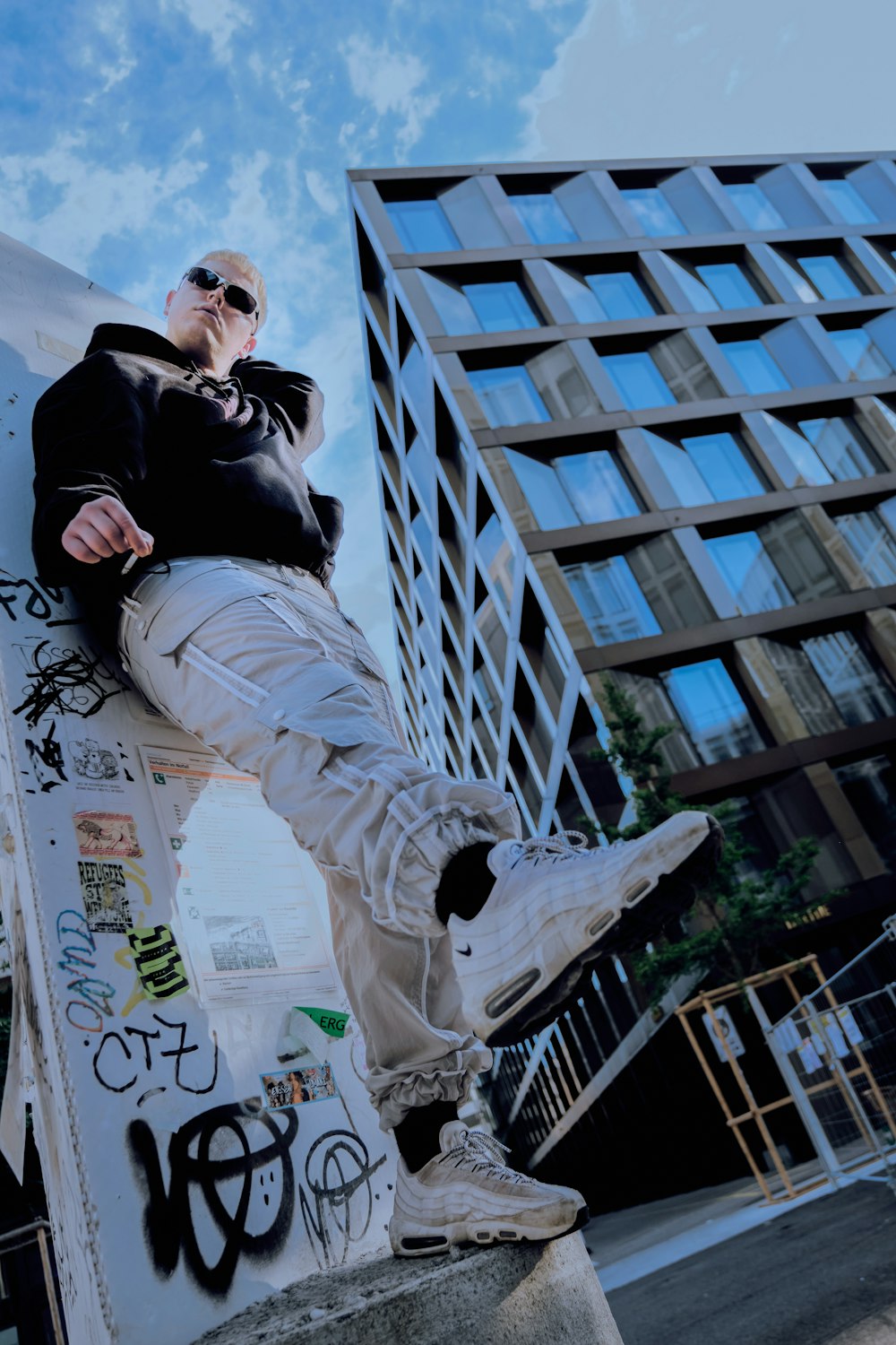 man in black jacket and white pants sitting on white metal fence during daytime