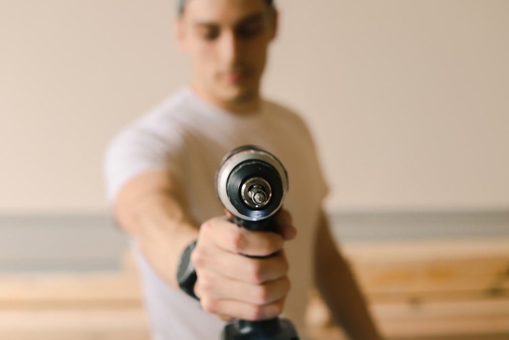 man in white crew neck t-shirt holding black and silver dumbbell