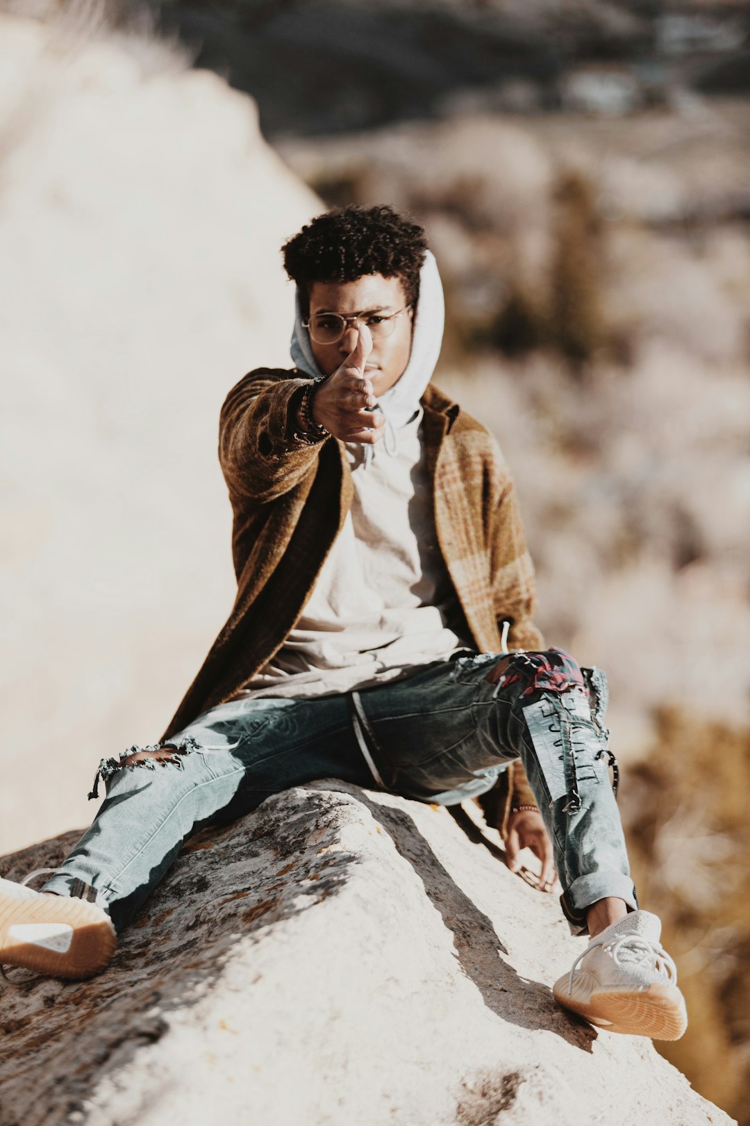 man in brown jacket and blue denim jeans sitting on rock