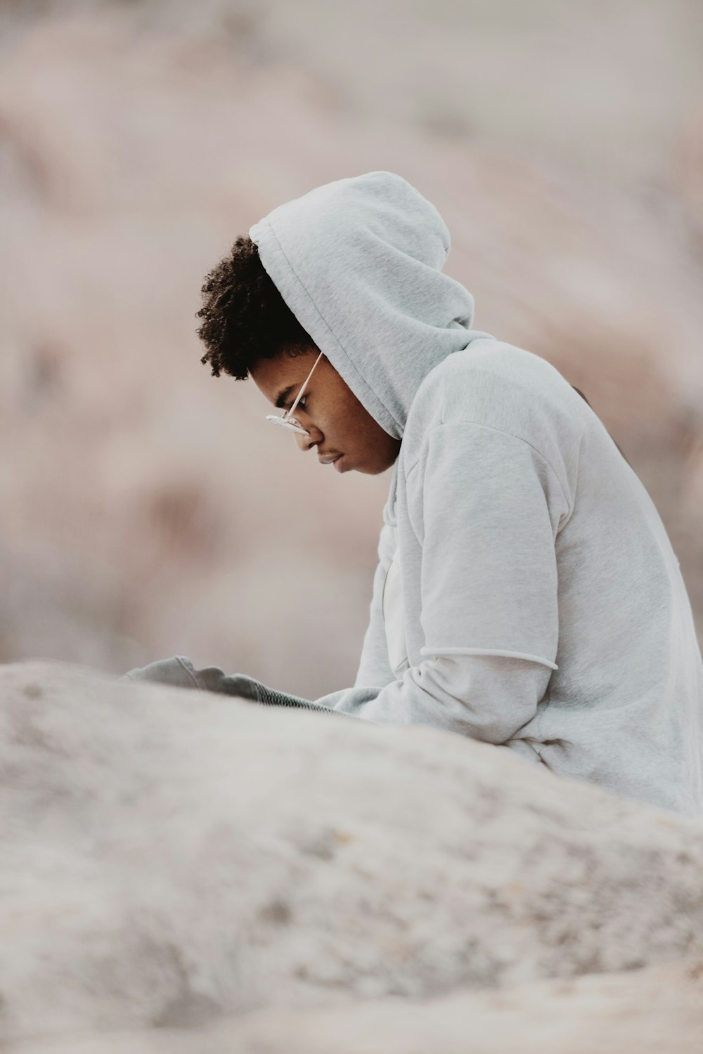 man in gray hoodie sitting on gray rock