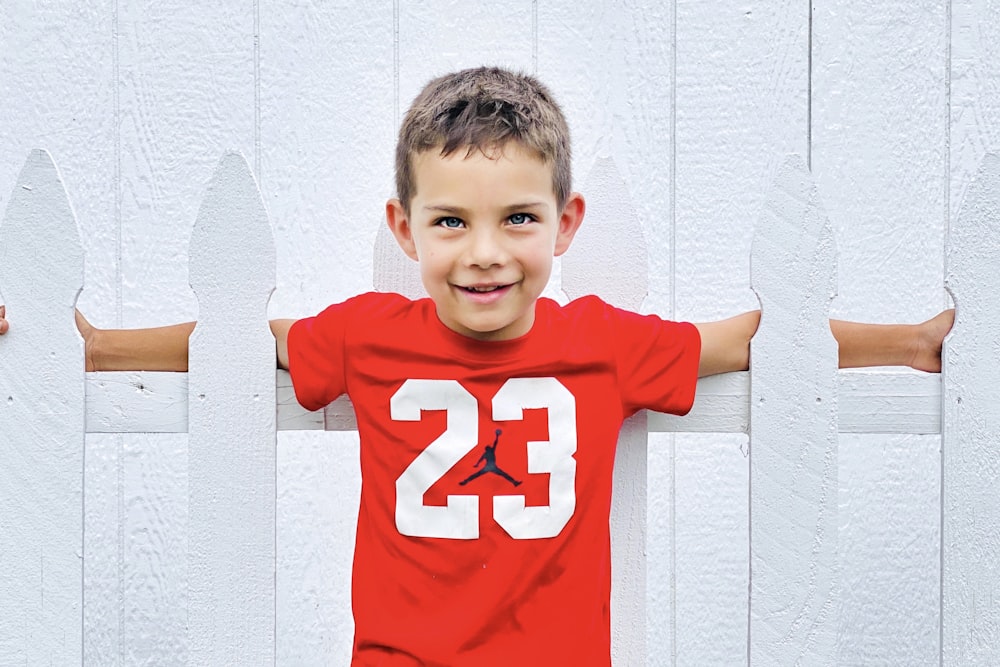 boy in red and white crew neck t-shirt leaning on white wall