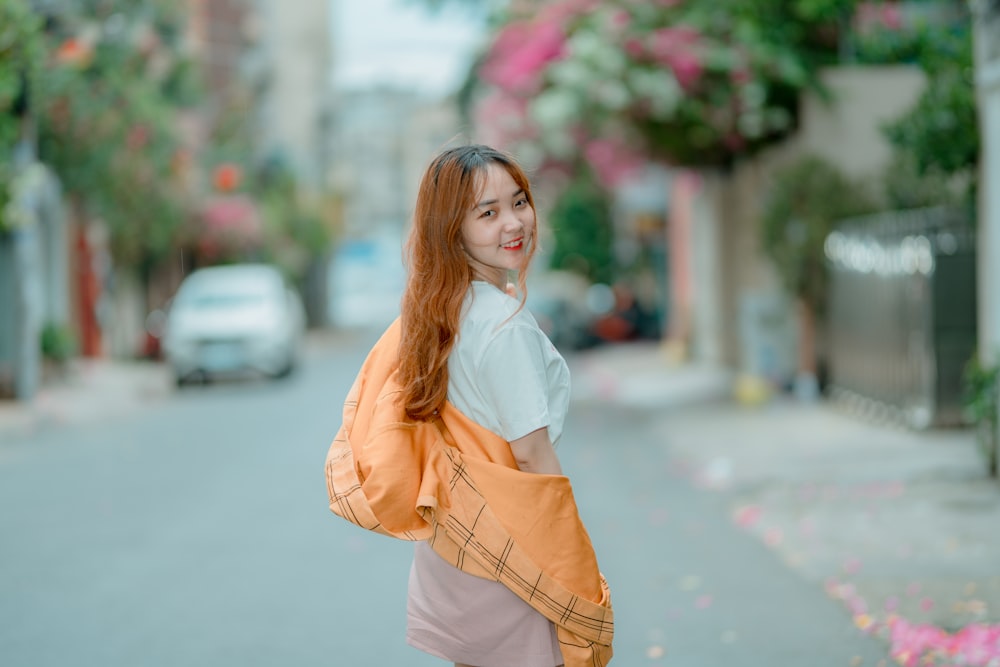 woman in white shirt and brown coat standing on road during daytime