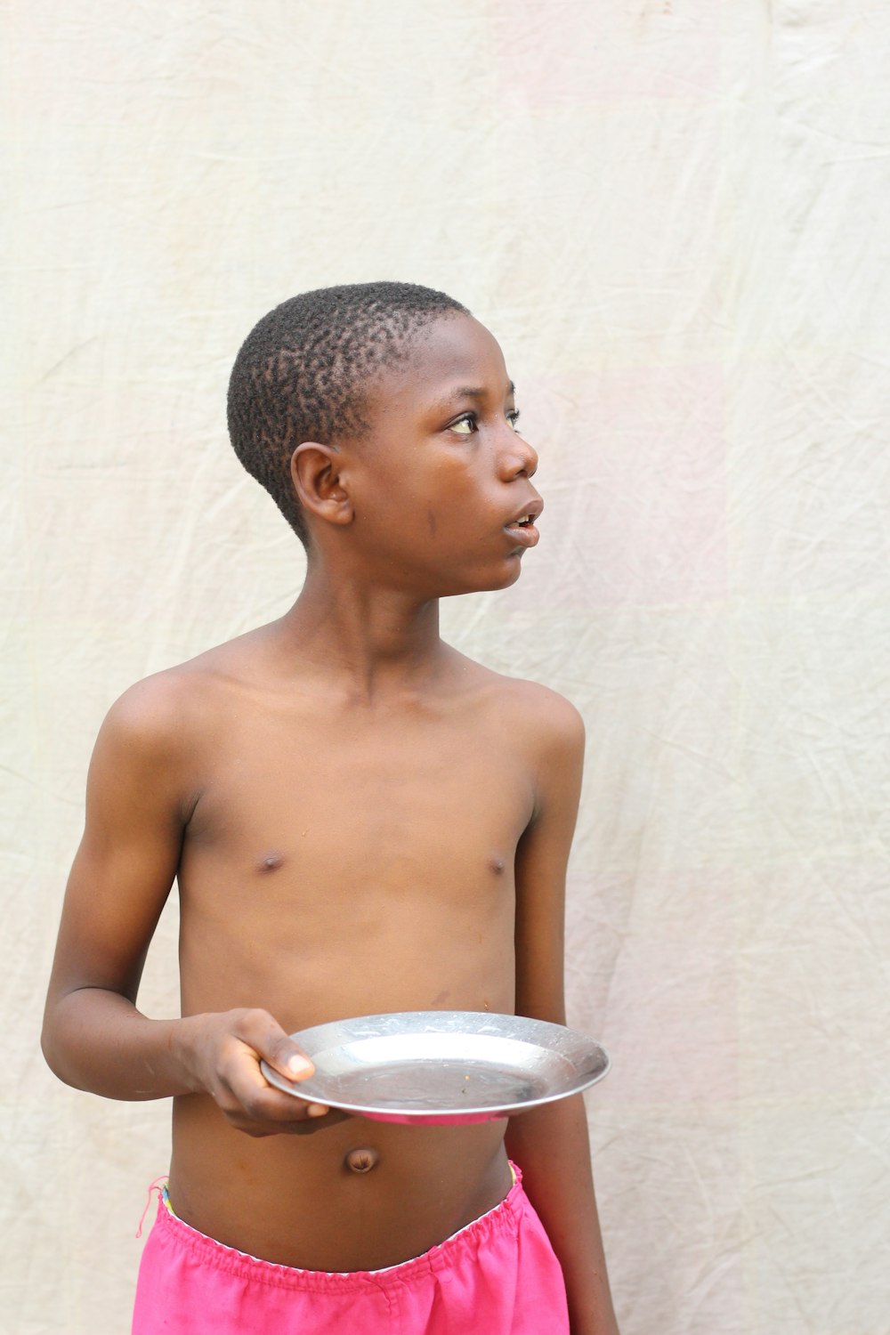 topless boy holding white ceramic bowl