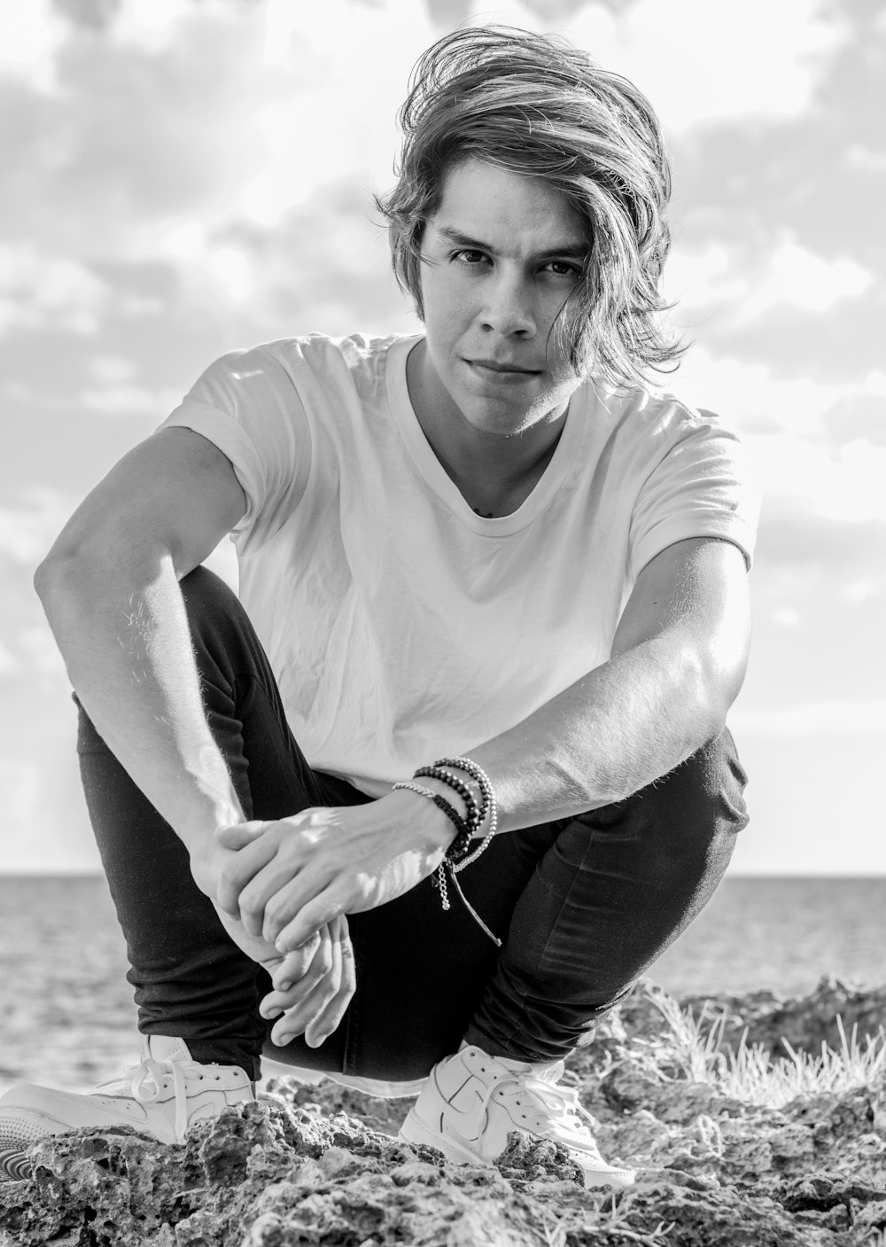 man in crew neck t-shirt and black pants sitting on grass field in grayscale photography