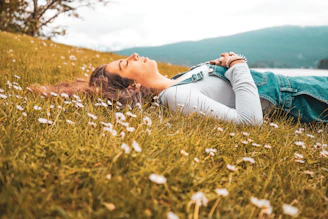 woman in blue long sleeve shirt lying on green grass field during daytime
