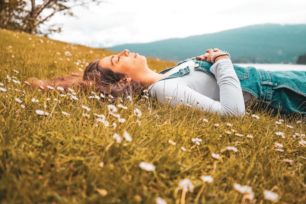 femme en chemise à manches longues bleue couchée sur un champ d’herbe verte pendant la journée