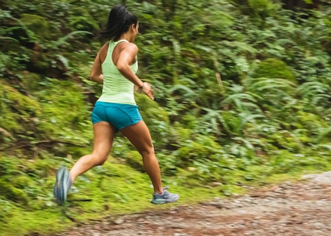 A woman jogging on a scenic trail surrounded by lush greenery, wearing vibrant sportswear.