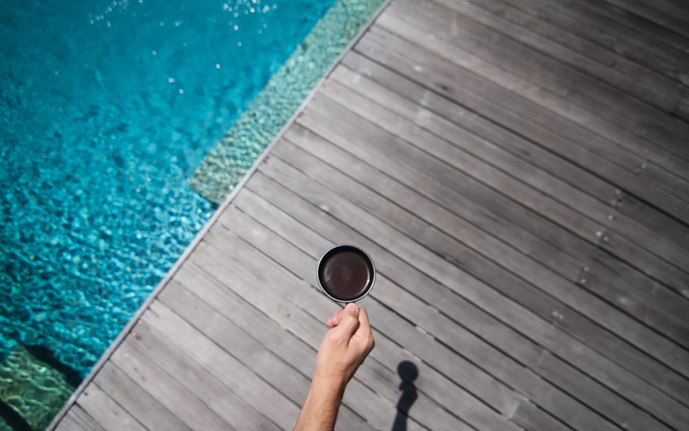 pessoa segurando caneca de cerâmica preta perto da piscina durante o dia