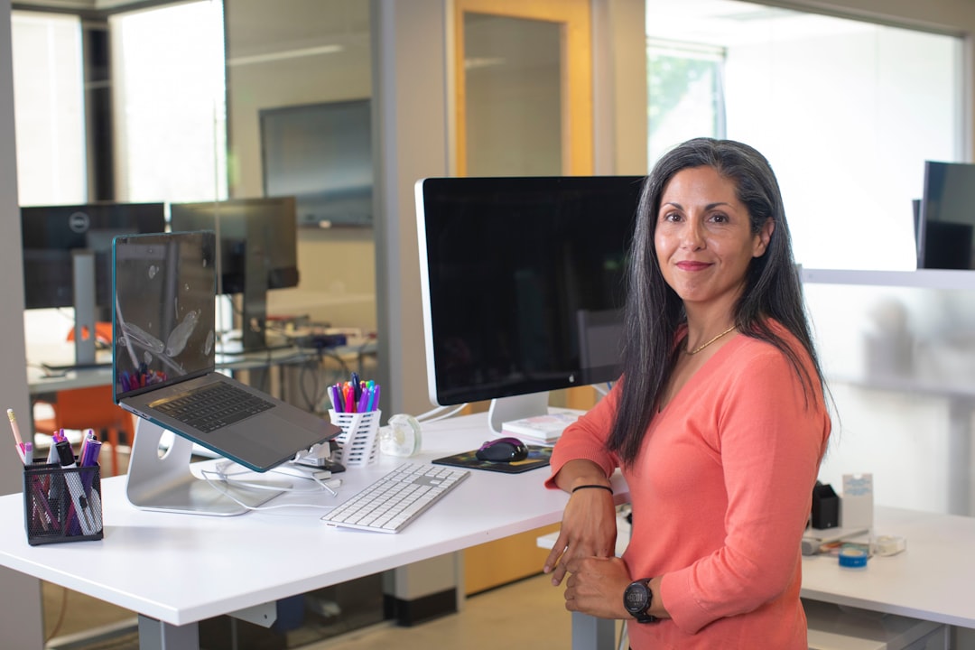 woman in orange long sleeve shirt sitting on chair, Sales woman at her standing desk working