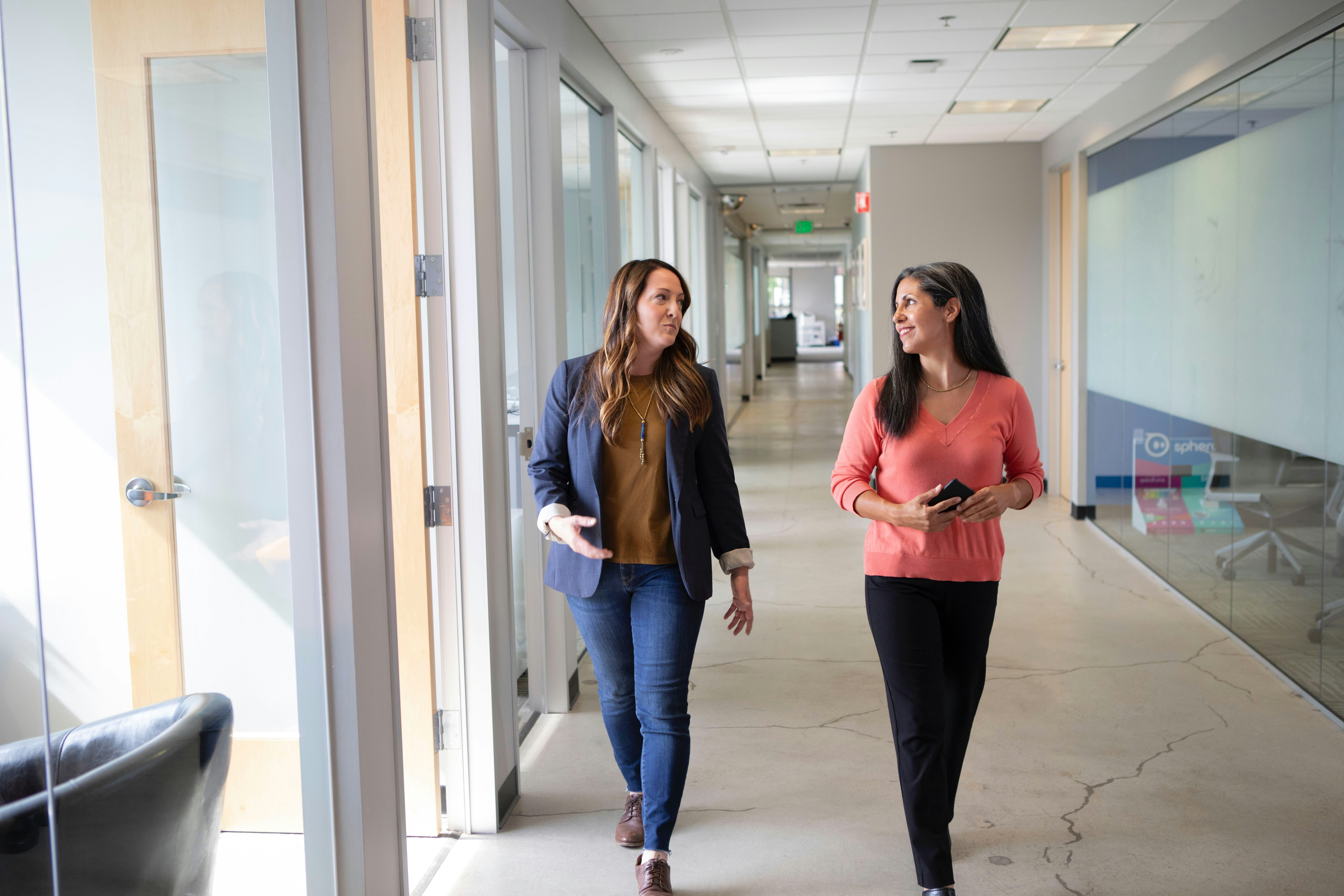 Two business women talking sales walking in office