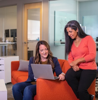 two women sitting on a couch looking at a laptop