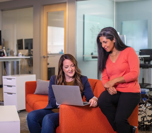 two women sitting on a couch looking at a laptop