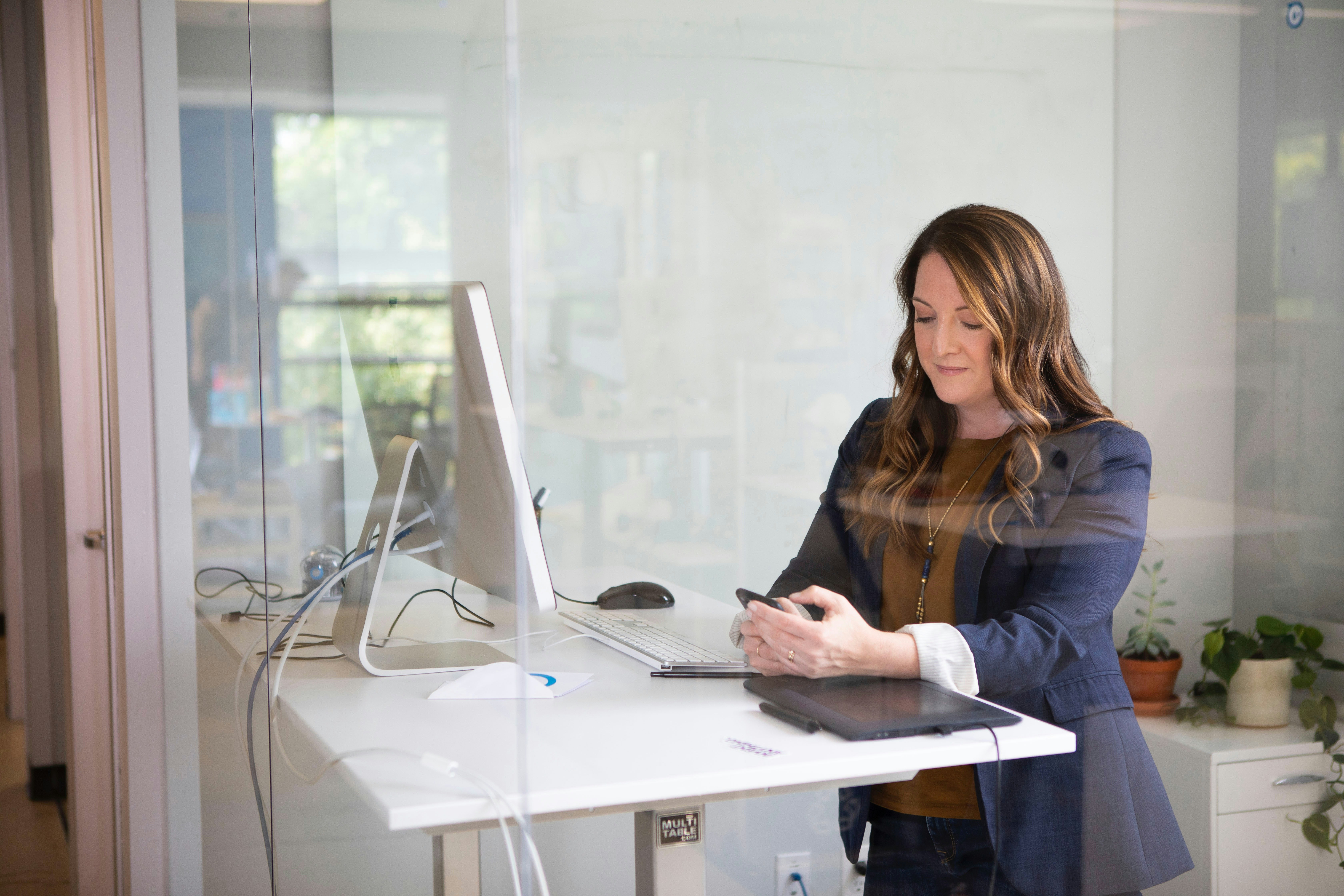 Sales woman checking her phone standing at desk with laptop