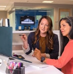 two women sitting at a table looking at a computer screen