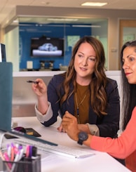 two women sitting at a table looking at a computer screen