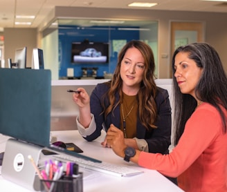 two women sitting at a table looking at a computer screen