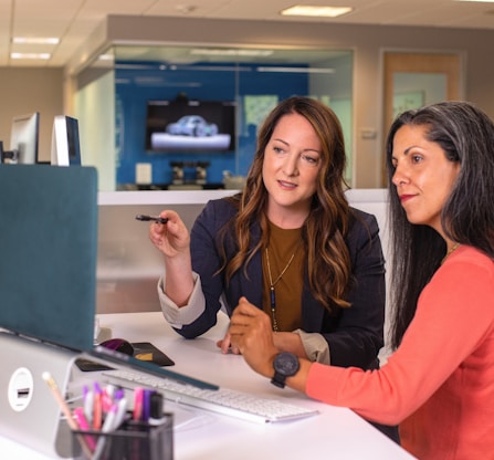 two women sitting at a table looking at a computer screen