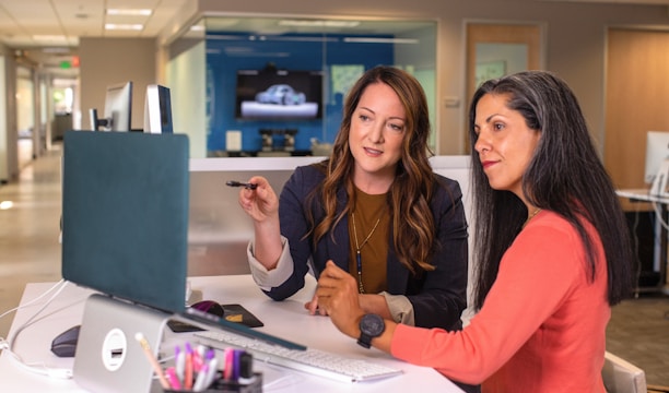 two women sitting at a table looking at a computer screen