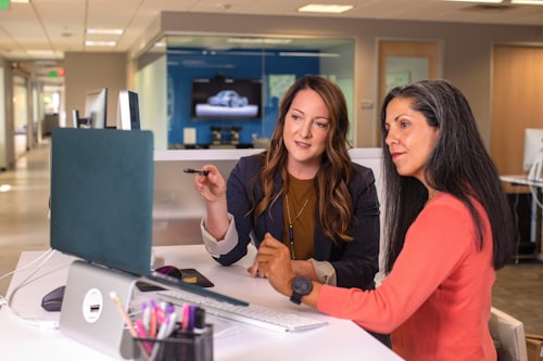 Two women looking at a monitor while sitting at a white elevated desk in an office.
