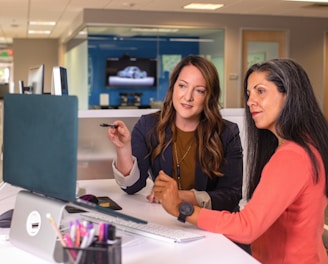 two women sitting at a table looking at a computer screen