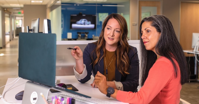 two women sitting at a table looking at a computer screen