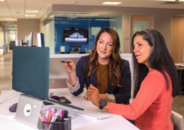 two women sitting at a table looking at a computer screen