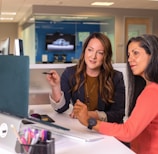 two women sitting at a table looking at a computer screen