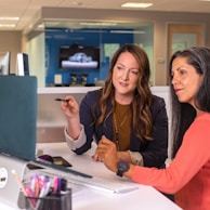 two women sitting at a table looking at a computer screen