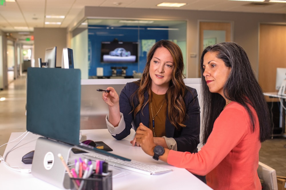 duas mulheres sentadas em uma mesa olhando para a tela de um computador