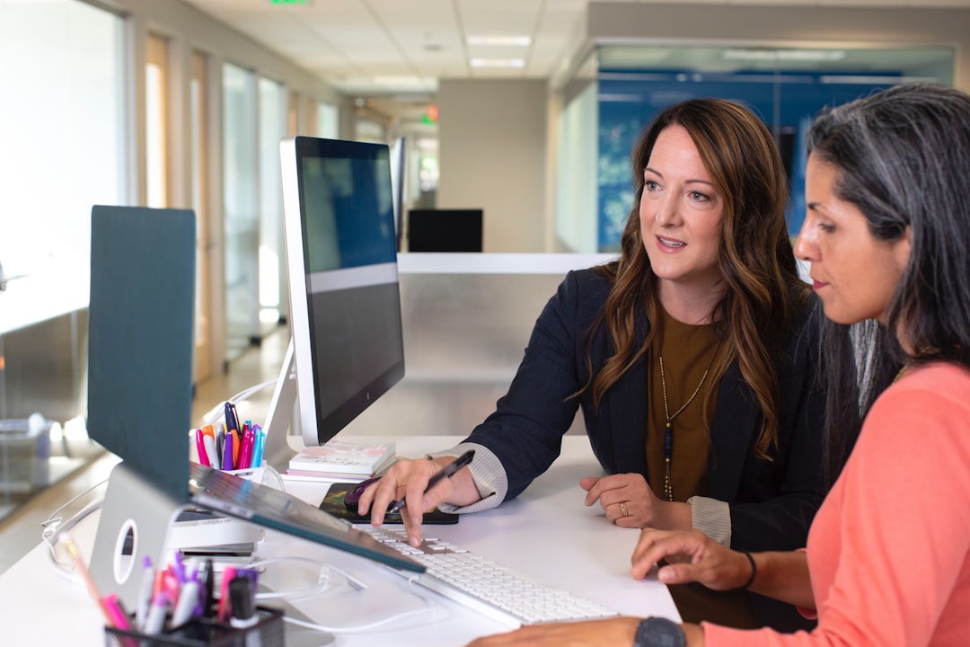 woman in black blazer sitting at the table, Two business women talking about sales at laptops