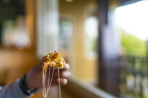 A hand holding a cheesy slice of pizza with strings of melted cheese stretching.