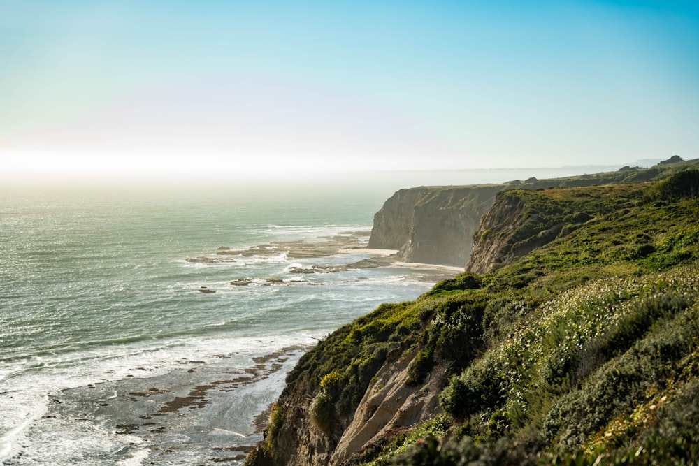 green grass covered mountain beside sea during daytime