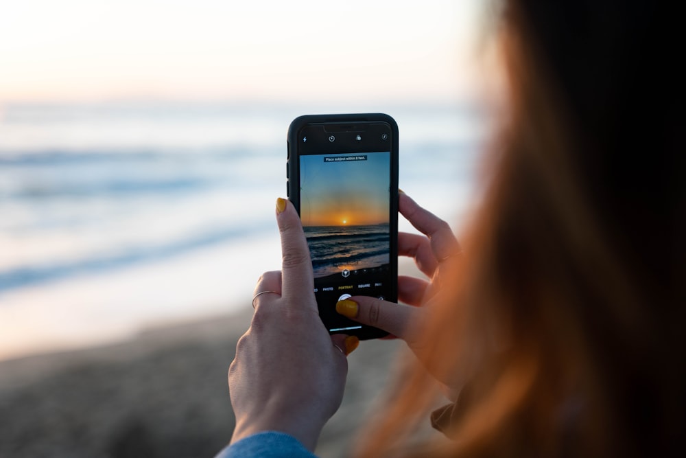 Person mit schwarzem iPhone 5 fotografiert den Sonnenuntergang