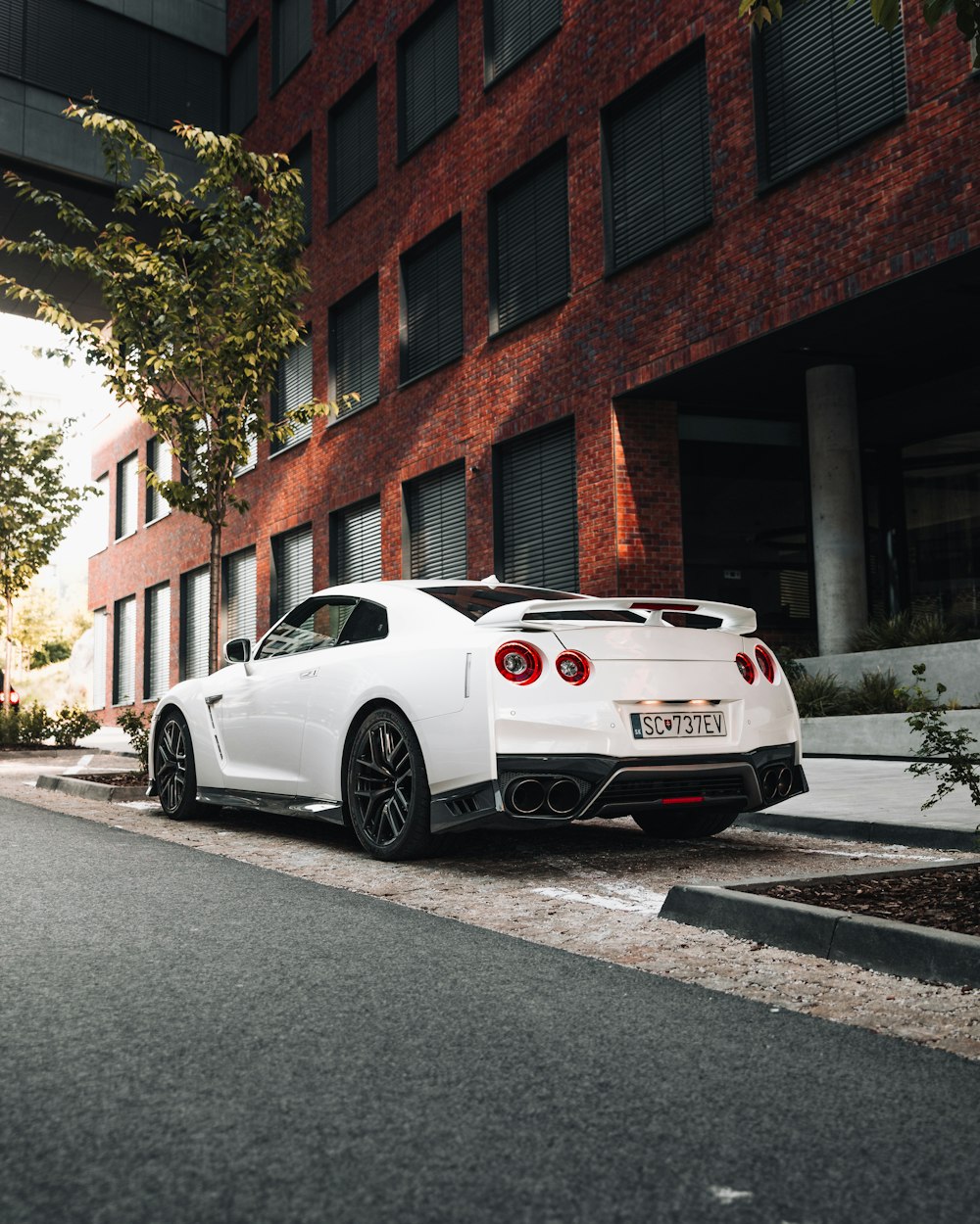 white coupe parked beside brown brick building during daytime